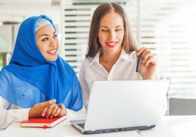 European woman and asian muslim woman working together on same p